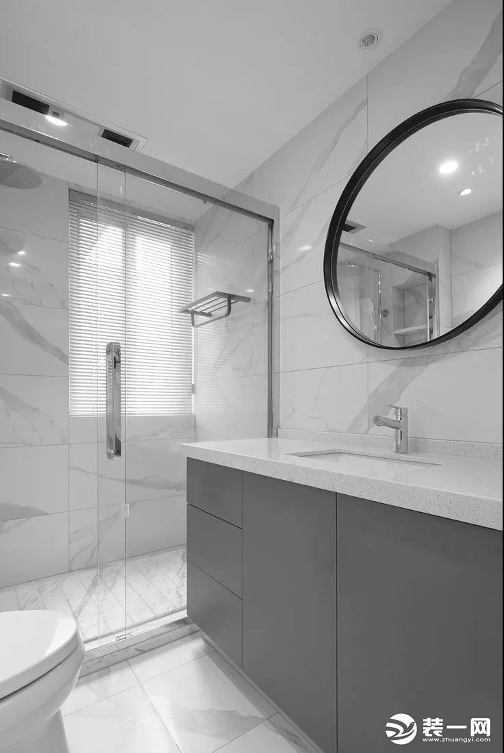 卫生间采用玻璃隔断作为干湿分区，大理石纹路的墙地砖清冷而纯净，结合黑框圆镜与灰色的浴室柜，打造出简约