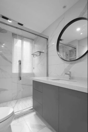 卫生间采用玻璃隔断作为干湿分区，大理石纹路的墙地砖清冷而纯净，结合黑框圆镜与灰色的浴室柜，打造出简约