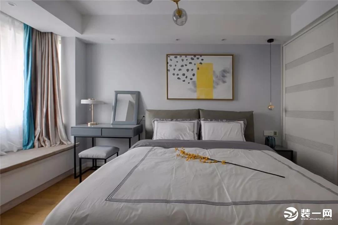 主卧室的配色同样是以灰色为主，窗帘选择了藕粉色和蓝绿色的拼色款式，看起来更为有趣。用梳妆台代替床头柜