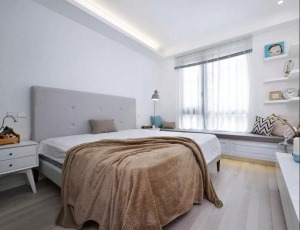 卧室以白色为主调，浅灰色布艺大床简约而舒适，咖啡色盖毯搭在床脚，轻松又随意。飘窗下方设置了整排的收纳