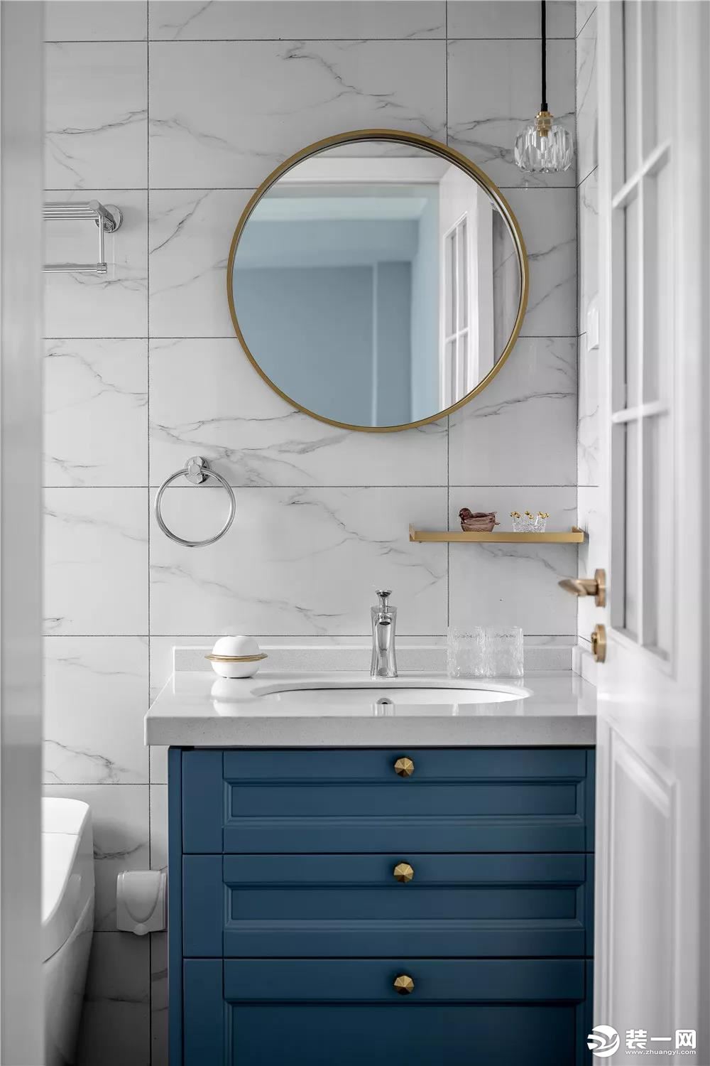 卫生间内铺贴了白色的大理石瓷砖，这款深蓝色的浴室柜让卫生间看起来更有格调。浴室镜和灯具都加入了铜质金