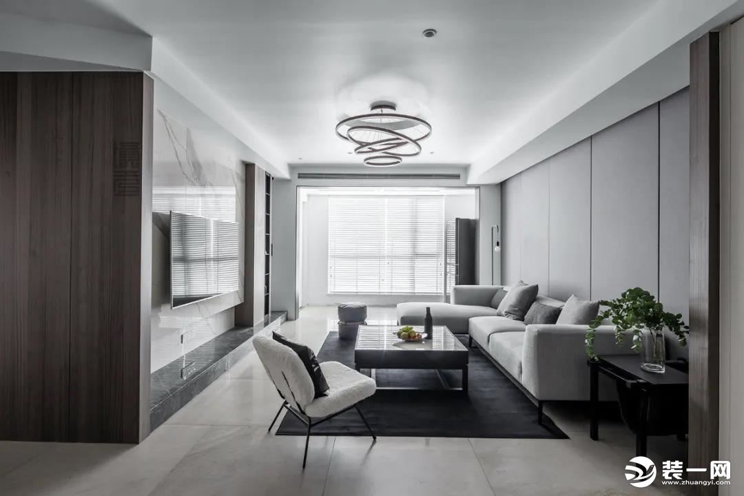 沙发墙用灰色的硬包作为背景墙，客厅中间布置灰色地毯与大理石台面的茶几，整体空间显得简约而又优雅华丽。