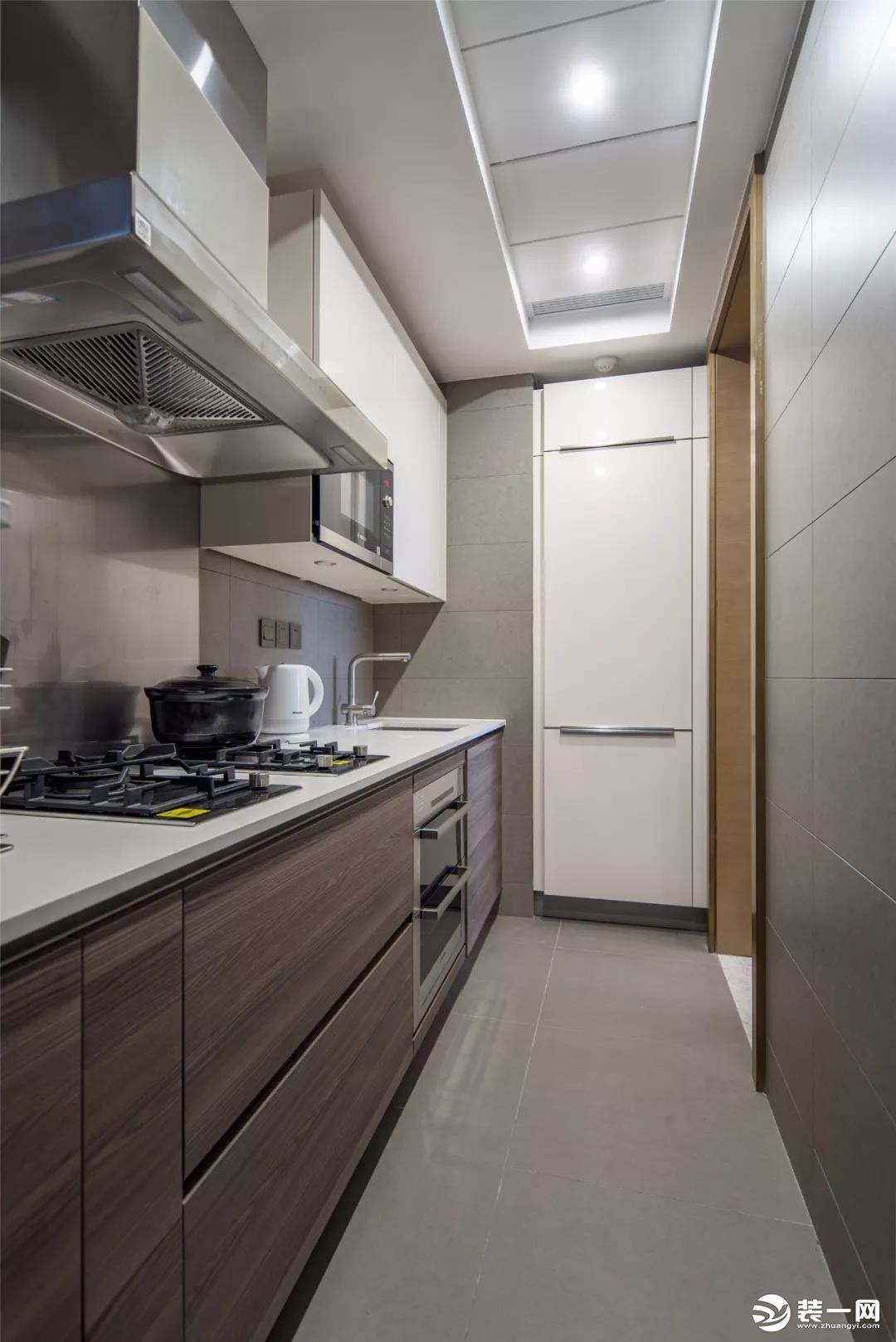 厨房的面积不大，还是一个狭长的空间，所以橱柜也是一字型的布局方案，设计师把冰箱嵌入到墙内，看起来更为