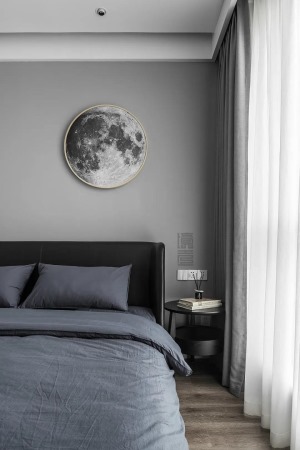 卧室在简约灰色的墙面基础，床头墙挂上一幅月球造型装饰画，布艺皮质床与黑色的床头柜，还有蓝灰色床单，整