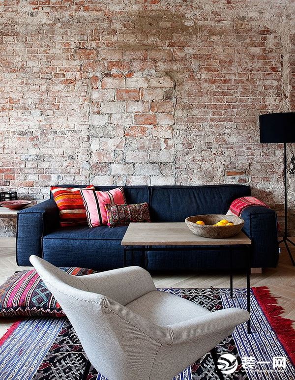 客厅红砖的背景墙，深蓝色柔软的布艺沙发，与编织地毯，红色与蓝色的搭配，红砖的呼应感受粗矿与随性，