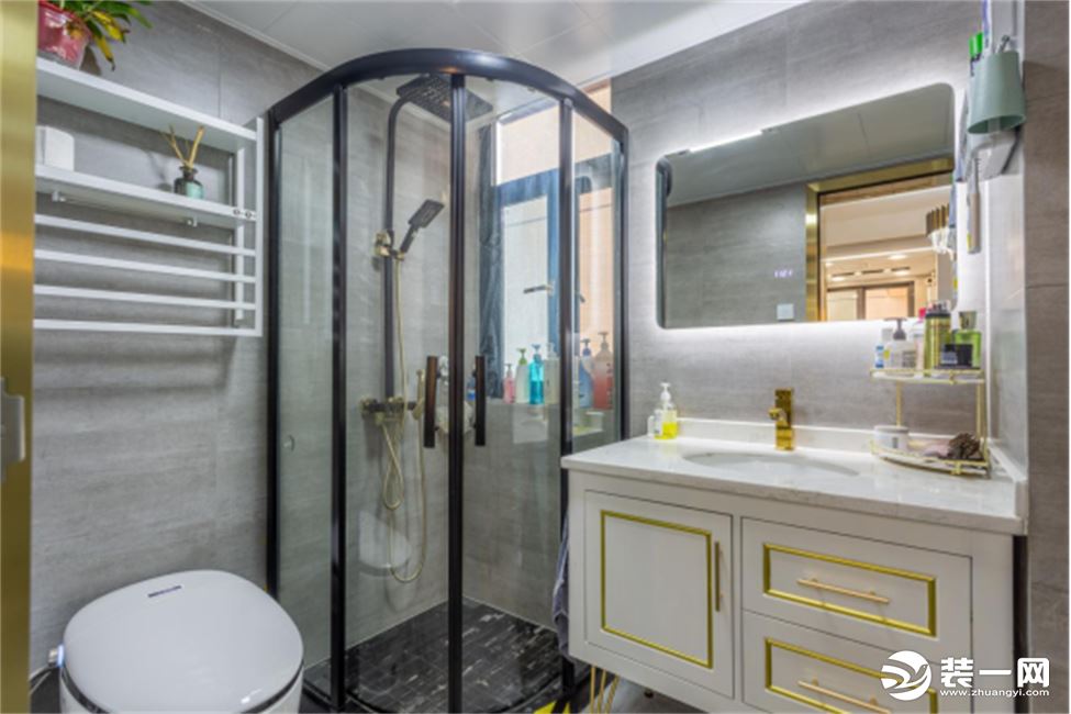卫生间墙地面通铺同色系瓷砖，搭配白色卫浴与黑色五金，黑白对比色的视觉层次清晰。自带光源的智能式浴柜镜