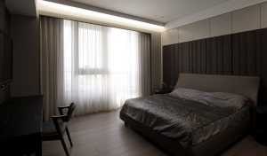 卧室在灰色床头墙基础，侧边加入木饰面的材质，搭配上灰色简约的布艺床，整体充满了简约的大方。