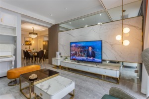 客厅的电视墙则是以地台+突出造型的设计，大理石花纹纹理再用金色不锈钢条收边，和电视柜的色系呼应，整体
