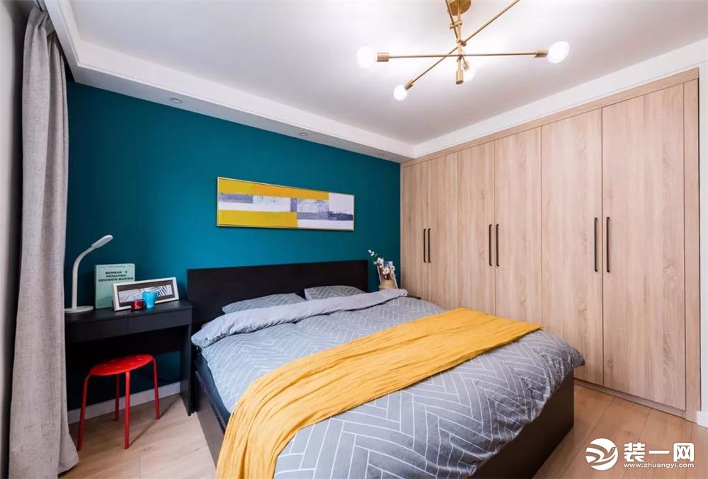 主卧 深蓝色的床头背景墙，木色的衣柜，黑色的床及书桌，用黄色的盖毯及挂画点缀，当然还有红色的椅子，营