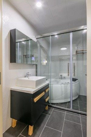 主卫灰色地砖+独特的白色粗糙纹理墙砖，搭配黑色的洗手盆柜与白色洗手盆，淋浴房还有一个小浴缸，为主人提