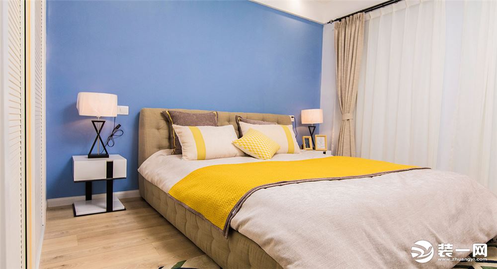 素色窗帘、布艺床头、简洁造型的床头灯搭配静谧的蓝色墙壁，整洁雅致。床品与墙面、地板的色调相互呼应，使