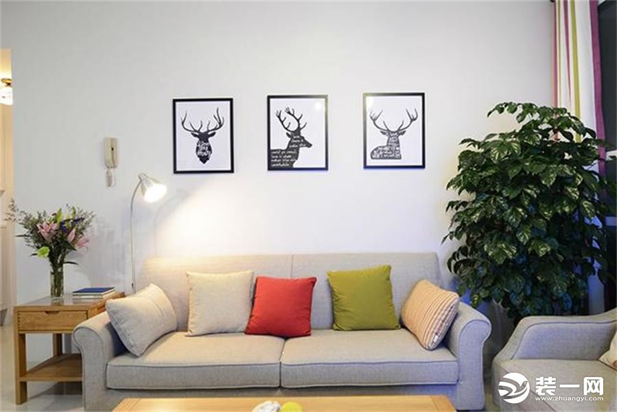 沙发是灰色简约的布艺沙发，背景墙上挂了麋鹿的画框，等孩子的写真照片到手就要挂上去了。