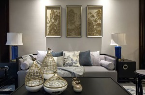 浅灰色的布艺沙发，搭配长方形黑色茶几，金色镂空的装盘，沙发墙上几幅金属质感的山水画，一个雅致的待客氛