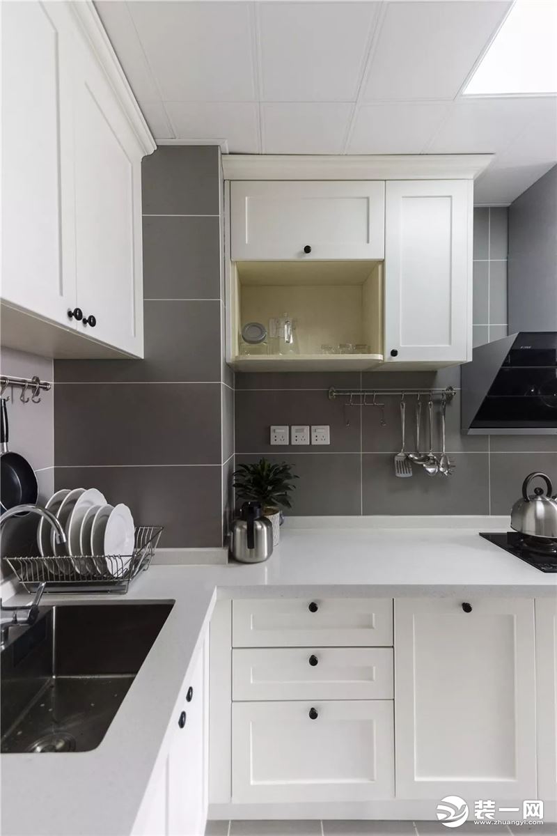 厨房内部的空间比较小，一个L型的橱柜搭配吊柜和挂杆、置物架等来满足厨房的收纳需求。以灰色和白色为主的