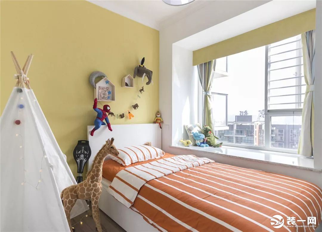 儿童房是以黄色作为主色，搭配橙色的条纹床品和浅绿色的窗帘、各种可爱、卡通的墙饰和玩偶