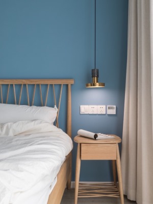 卧室：蓝色墙面与木质床具的搭配十分和谐，黄铜吊灯线条利落，整个空间利落静谧。