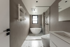 卫生间是干湿分离设计，兼顾淋浴区和泡澡区。灰棕色的硅藻泥质地墙面看起来十分的有质地，地面是颗粒感十足