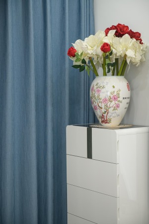 电视机旁一个白色的定制收纳柜，，上方放置一个中式花瓶，白色与红色的玫瑰花相互映衬着，带来视觉的冲击，