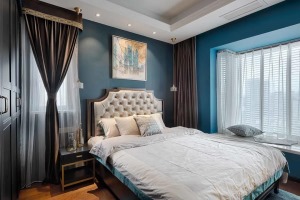 主卧在蓝色的墙面空间基础，搭配黑色的衣柜、床头柜，摆上布艺靠背的美式床，简素的床单与床头挂画，也是显