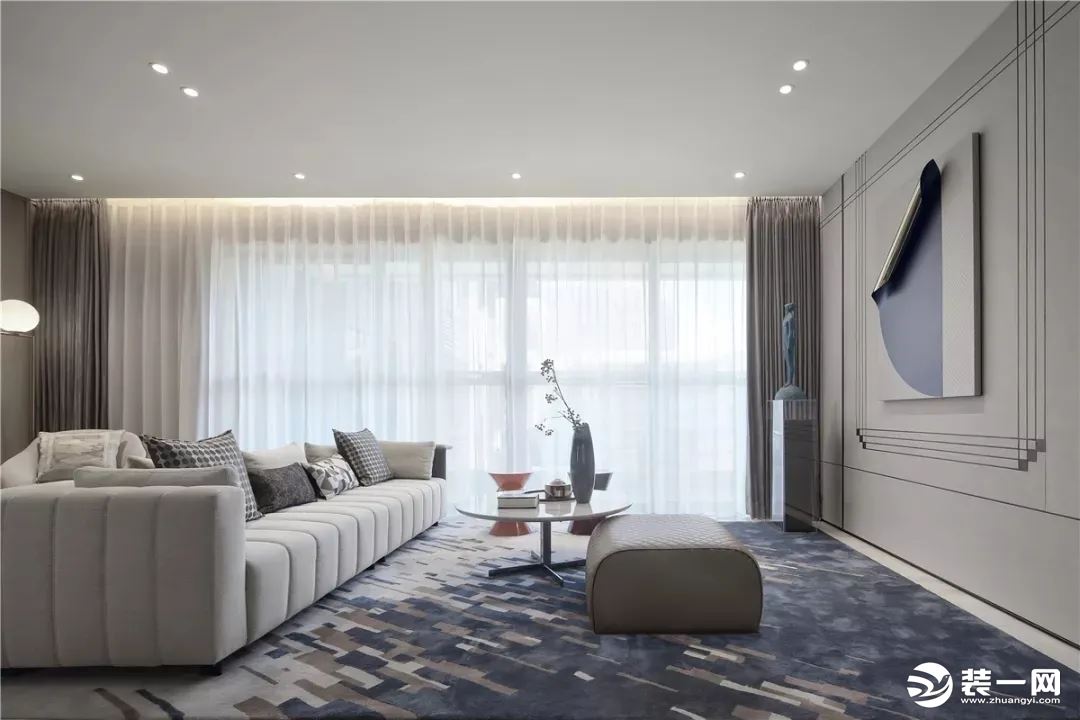 客厅垫着大面积的蓝色调地毯，布置现代舒适的布艺沙发，还有大理石材质的圆茶几与小鼓凳，简洁的电视墙以硬