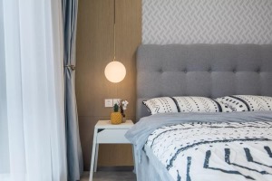 ▲次卧床头背景墙有木饰面+壁纸的非对称设计，左侧床头柜上一盏球形的吊灯，搭配灰色床与白色带灰色图案的