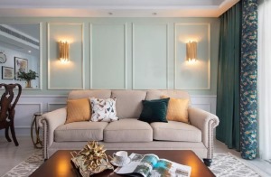 米色布艺沙发造型简约，柔软温暖，配以橙色与墨绿色抱枕，细腻而复古。