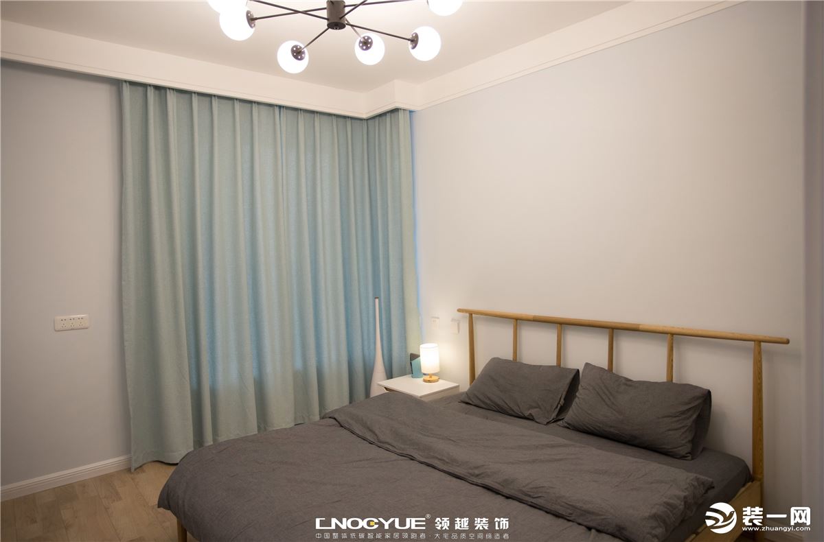 木色地板、灰色床组、奶白色衣柜、浅蓝色窗帘，在沉稳的色调和用材之下，暖光灯饰室内点缀...