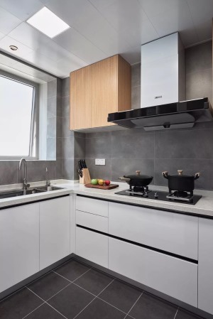  厨房墙地面通铺灰色系瓷砖，搭配白色橱柜以及木色吊柜，结合简洁利落的黑色线条，整体简约而时尚。