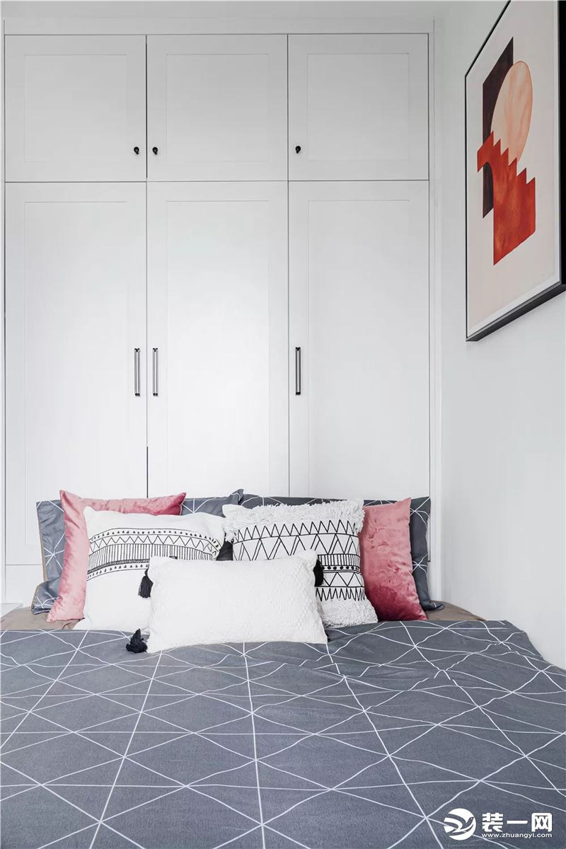 ▲ 次卧面积较小，靠墙安装了定制的榻榻米床，搭配灰色床品与粉色抱枕、挂画，呈现出简约而优雅的氛围感。