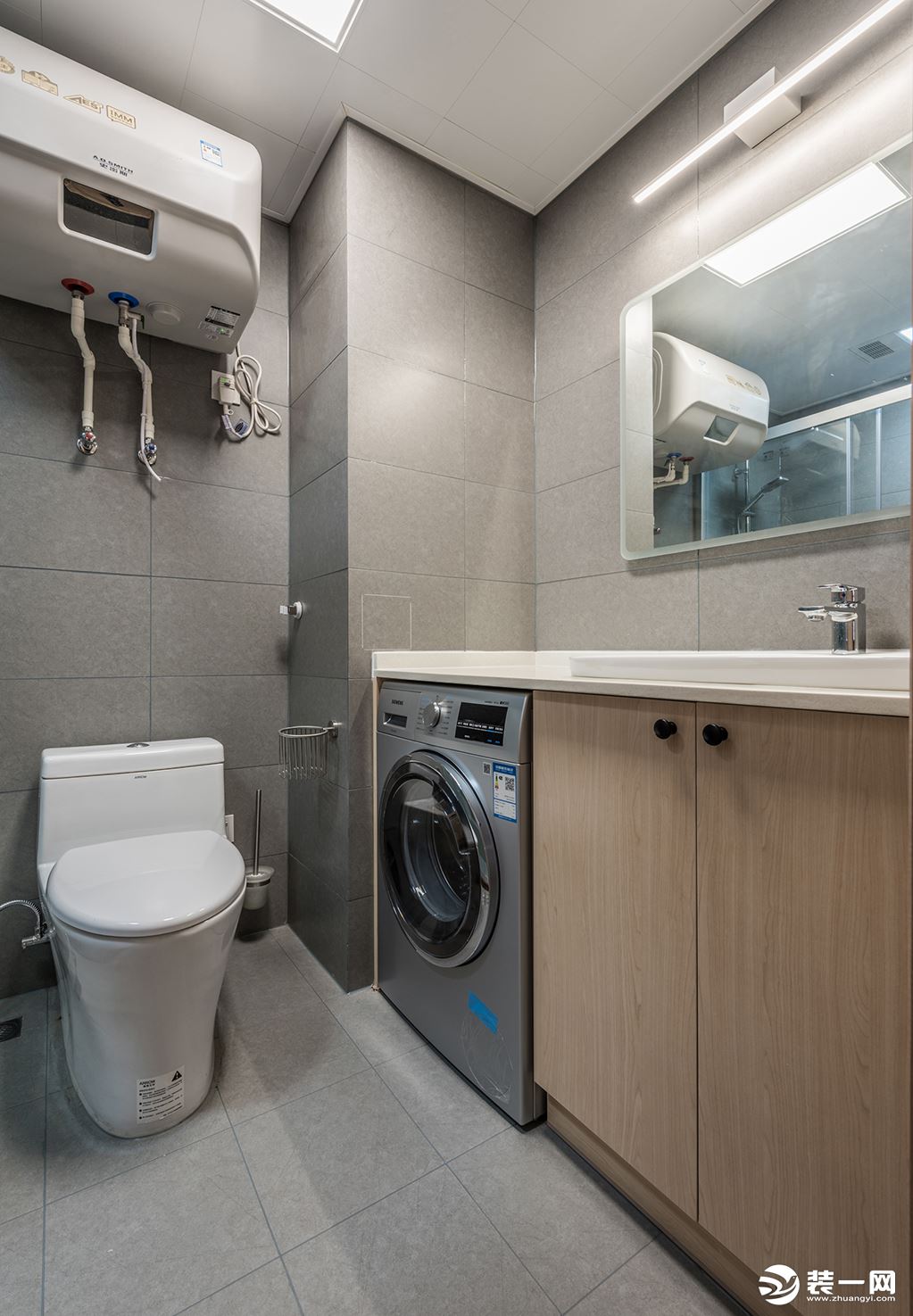卫生间采用嵌入式洗衣机。灰色的墙体设计和木色的柜门设计，清冷纯粹，增加了不少质感