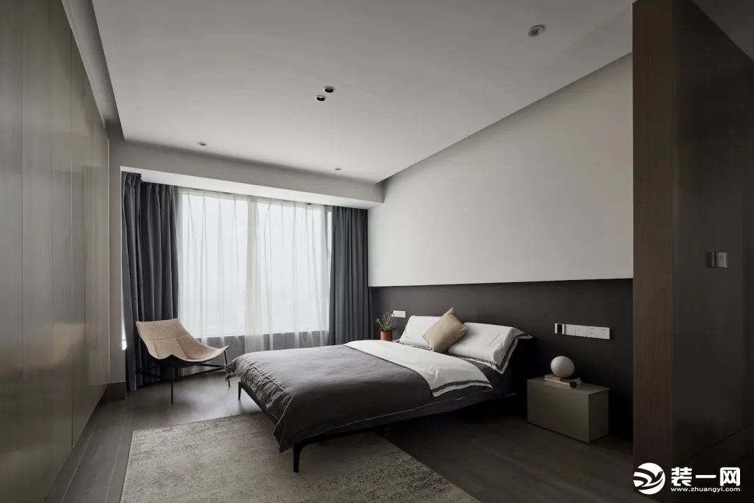 卧室在无主灯的空间基础，床头墙以深色墙脚+白色墙身的层次感下，布置舒适的灰色床铺，呈现出一种舒适自然