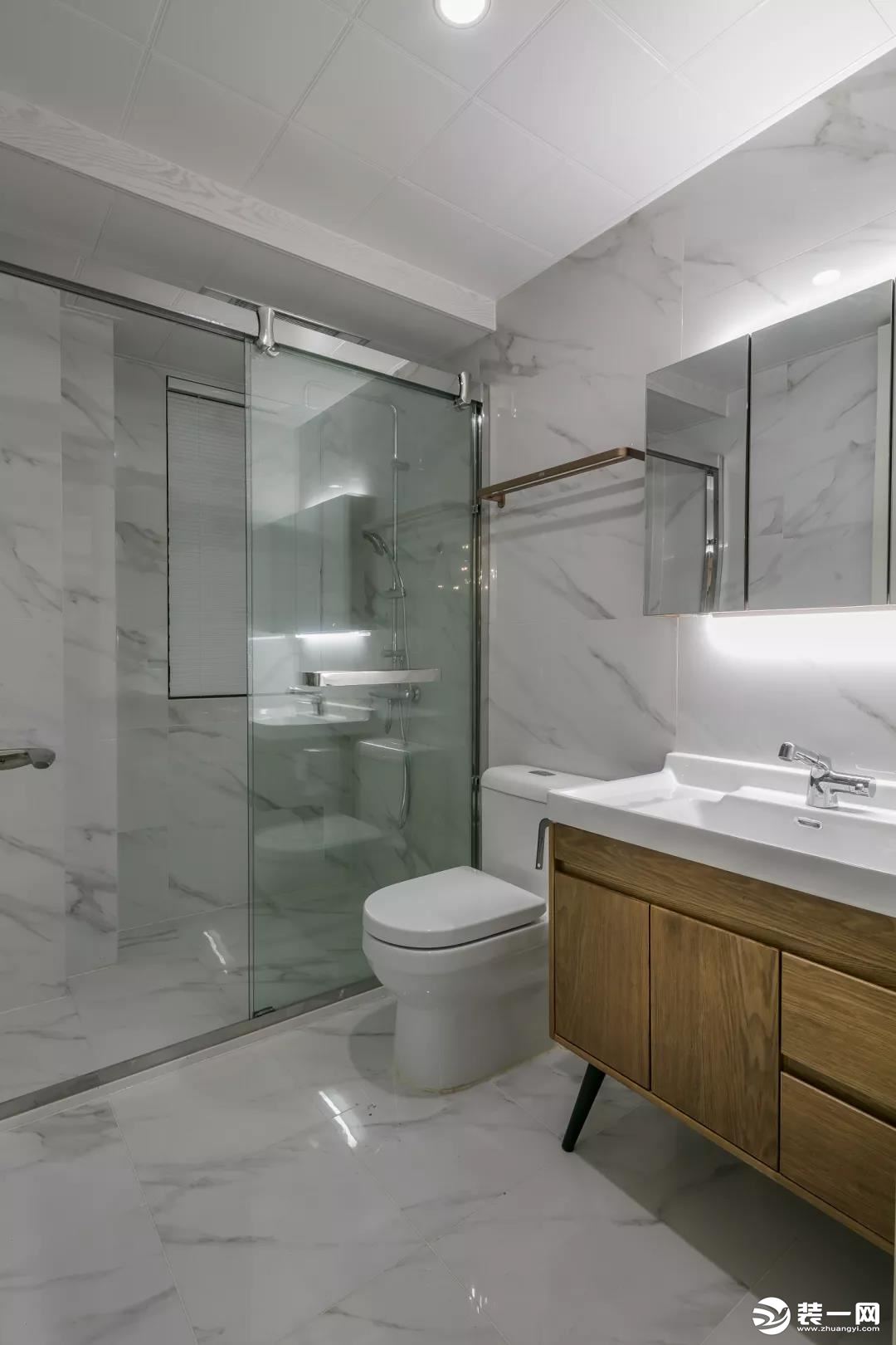 客卫以爵士白的墙面地面，玻璃隔断了淋浴区域，结合木质洗手盆柜