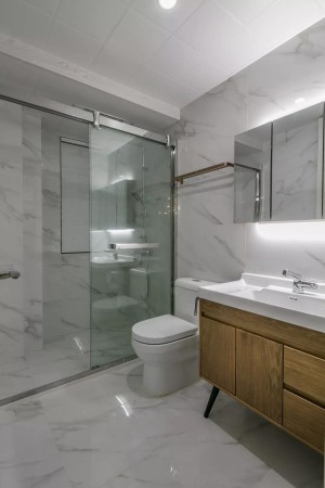 客卫以爵士白的墙面地面，玻璃隔断了淋浴区域，结合木质洗手盆柜