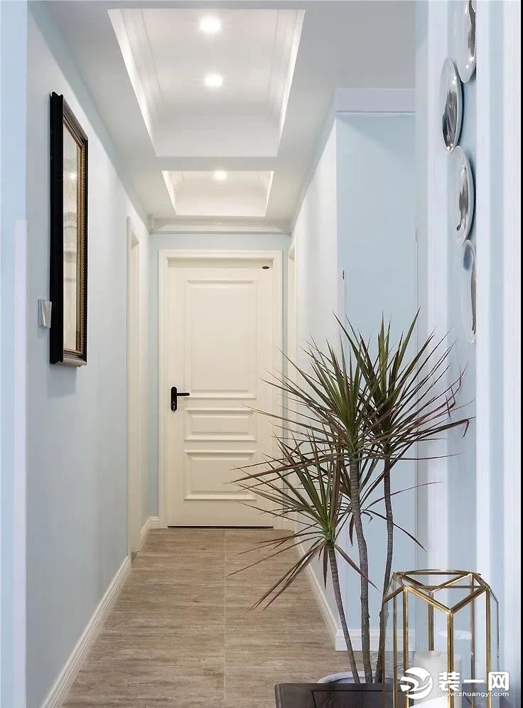 走廊空间同样以蓝白两色为基调，墙面以挂画和挂盘为装饰，一盆绿植增添一份清新与活力。