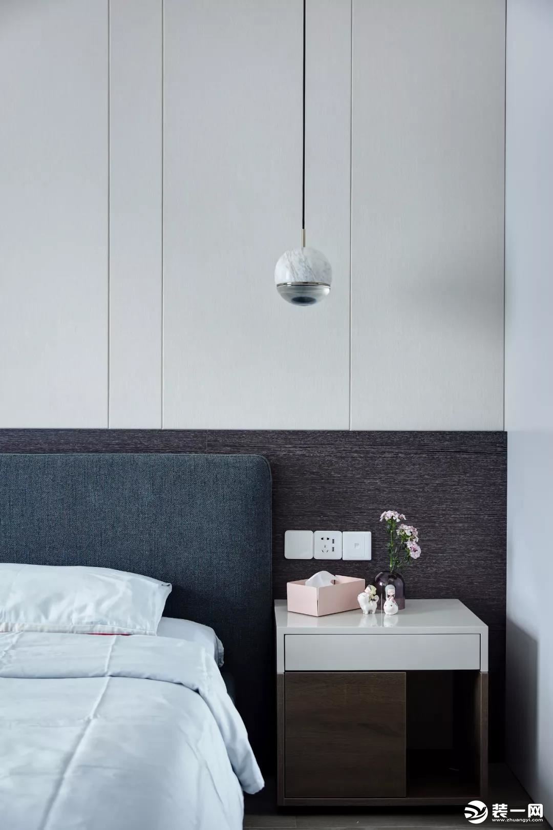 卧室床头墙以灰色+白色硬包的背景墙，结合一张灰绿色布艺靠背床，床头柜的精致小摆饰，都让空间显得格外的