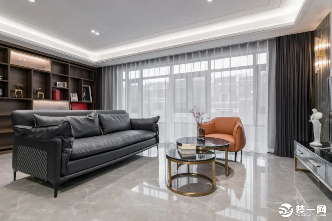 客厅空间以灰色大理石通铺地面，搭配灰色皮沙发，还有金属+黑色大理石台面的双拼茶几，边上一张橙色沙发椅