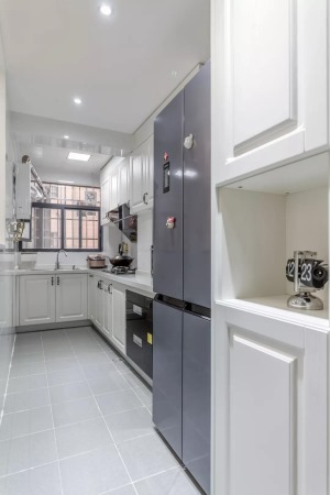 廚房是長方形的，因此做了比較流行的L型櫥柜，提前預留好雙開門冰箱的位置，灰色地板搭配白色櫥柜，顯得十