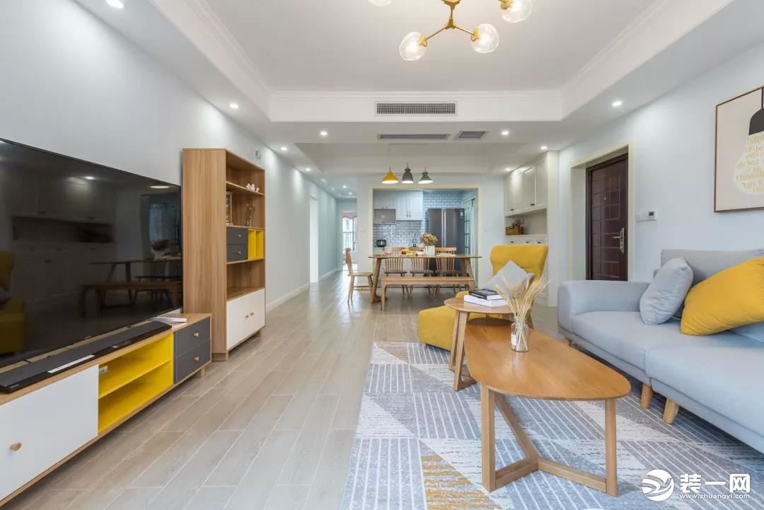 灰色布艺沙发，搭配木质椭圆小茶几，还有舒适的地毯，电视墙。白、黄、灰色的组合