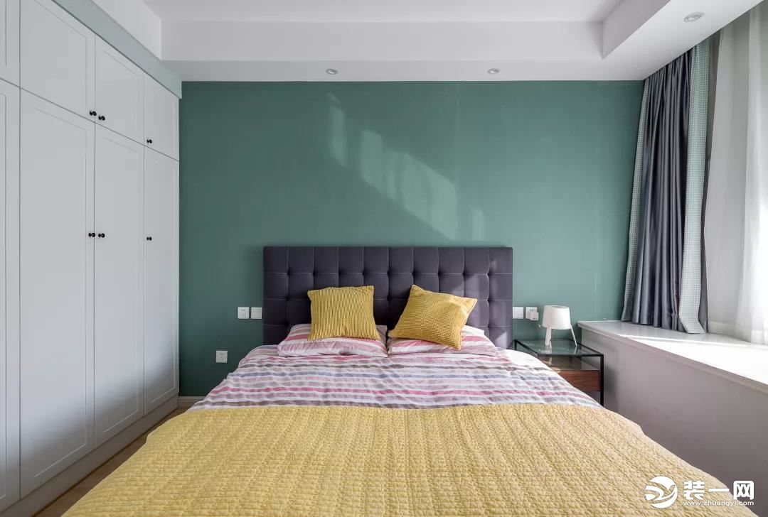 主卧室的背景墙的墨绿色非常漂亮，深灰色的床头靠背，黄色的床上抱枕，纯白色的飘窗和衣柜，很简约舒适。