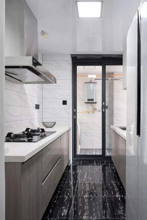 厨房还连通了生活阳台，所以橱柜也做了双一字形的布局方案，黑色的大理石地砖搭配白色的墙砖