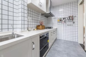 厨房以浅灰地砖+白色小砖墙面，一字型的操作台，雅白的橱柜，在侧边的墙面还加入了实用的厨具纳架