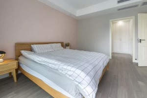 主卧床头墙是淡粉色的，侧边墙面则是浅灰色，搭配木质床与简约的床单，整个空间充满了舒适自然的气息。