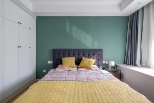 主卧室的背景墙的墨绿色非常漂亮，深灰色的床头靠背，黄色的床上抱枕，纯白色的飘窗和衣柜，很简约舒适。
