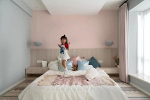 儿童房床头墙是粉色的，靠背的木质护墙板与床头柜连成一体式的，侧边墙面则是蓝灰色的，搭配上温馨可爱的床
