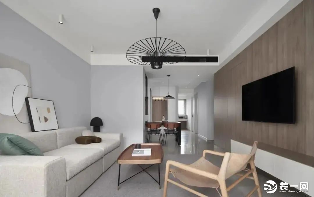 客厅空间整体以灰色系为主，再配上灰色地毯、米白色布艺沙发、木质茶几、木饰面的电视墙、木色茶几与休闲椅