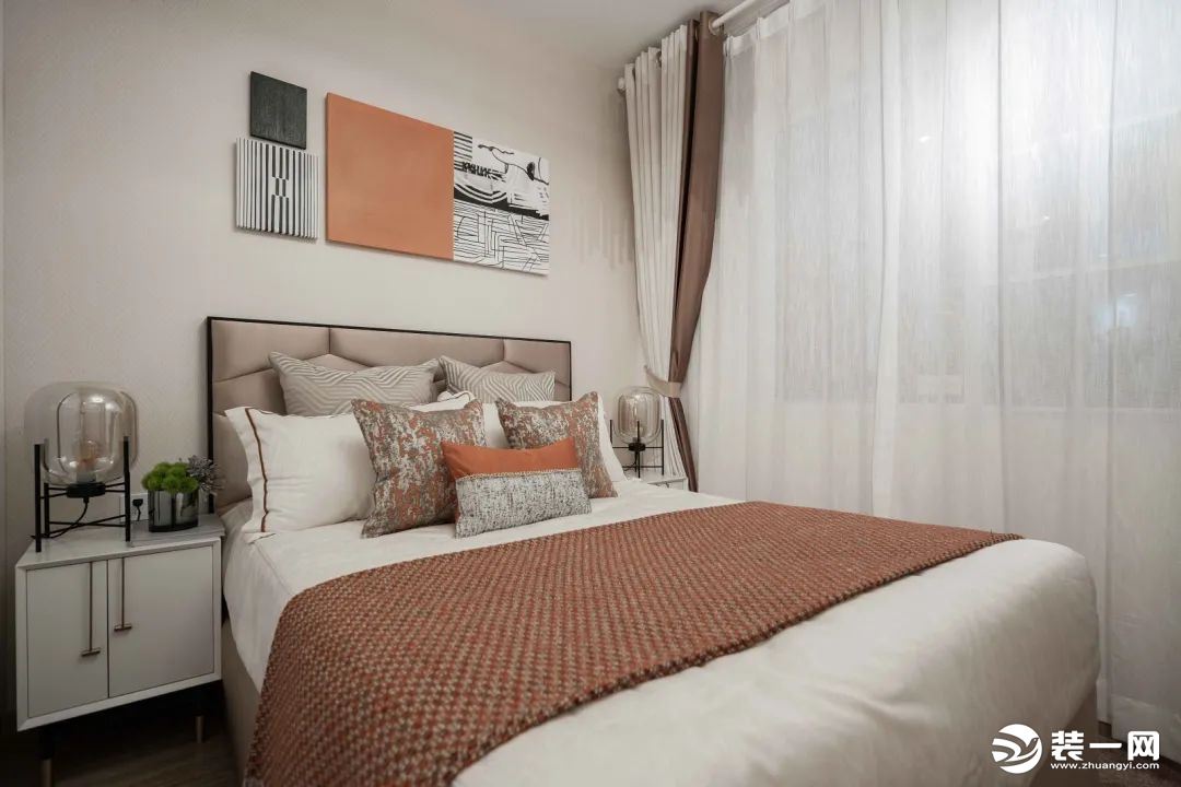 次卧在浅咖色墙面基础，床头墙挂上几幅黑白橙色的几何线条装饰画，皮艺床上布置白色与橙色的床品，两侧象牙