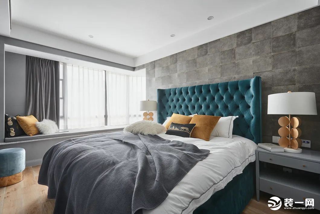 卧室床头墙贴上灰色仿古砖材质的背景墙，布置一张宝蓝色的皮艺床，布置灰白配的床单，两侧还有灰色的床头柜