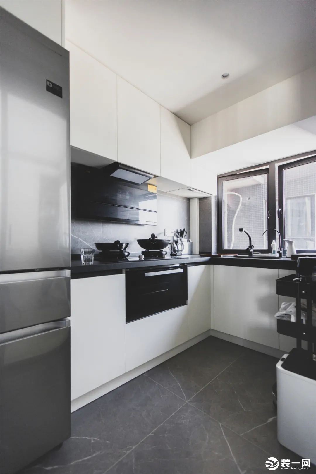 厨房，经典的黑白灰搭配，看上去简洁时尚。采用了L型的橱柜布局，并将冰箱嵌入进去，空间的极致利用。