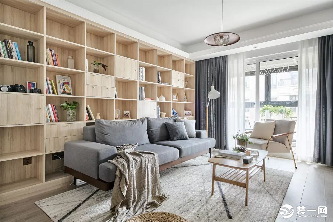 客厅整体以灰白色与木质为主调，灰色布艺沙发简约有质感，后方是一面木质书架墙，格外的实用有情调。