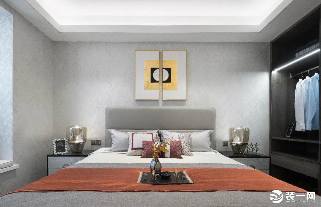 卧室墙面贴上灰色墙布，床头墙的两幅长条装饰画拼一起后，形成一个正方形的图案，两侧对称的床头柜上也是布